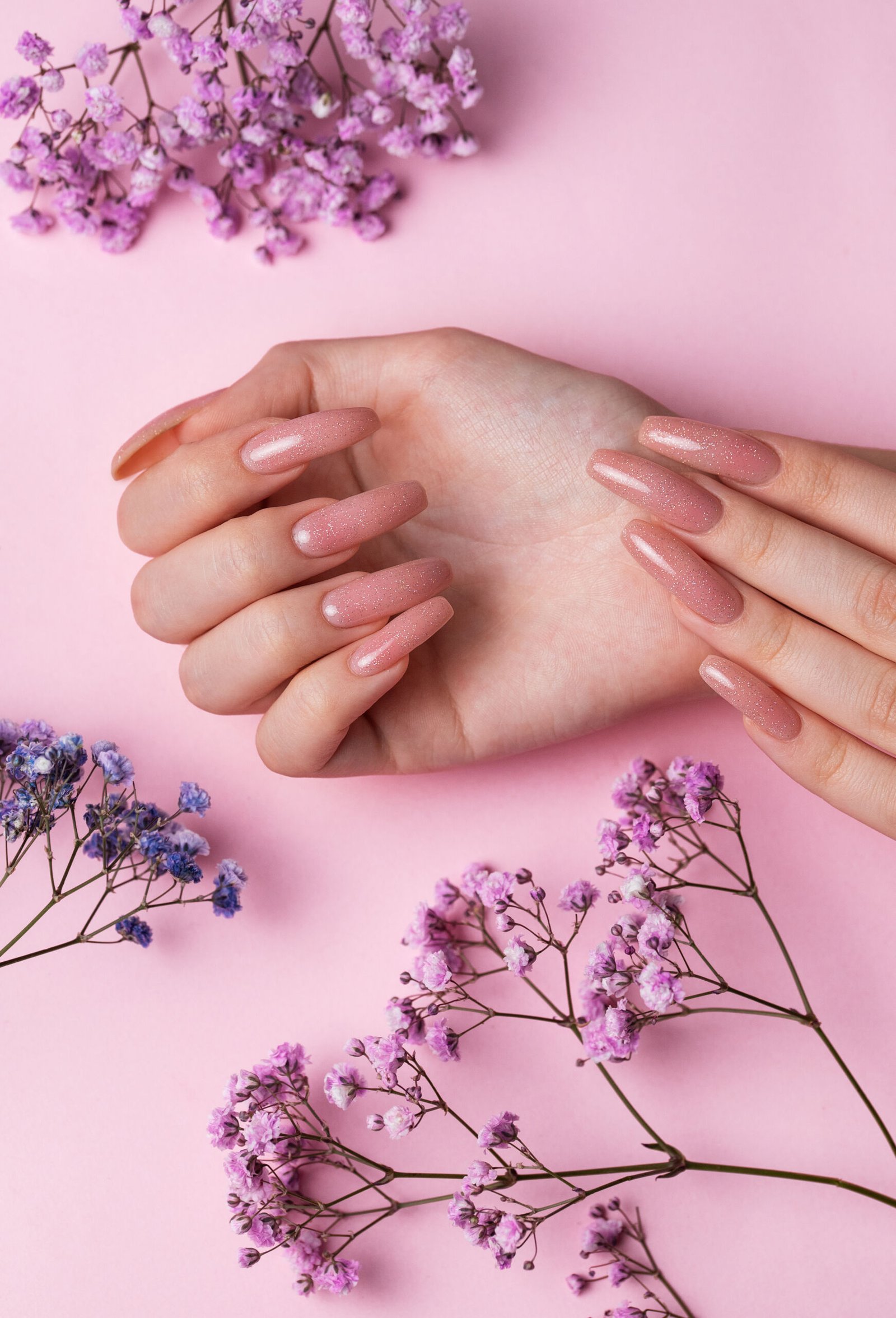 Female hands with pink nail design  hold gypsophila flowers. Pink nail polish manicure on pink background